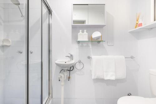 Un baño blanco con ducha y lavabo. en Hanks Corlette House, 49 Pantowora St - pet friendly, air con, boat parking, Wi-Fi, en Corlette