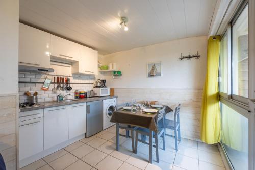 une cuisine avec une table et une petite cuisine avec des placards blancs dans l'établissement Le Petit Cocon Marin - Appt à 200m de la plage, à Courseulles-sur-Mer
