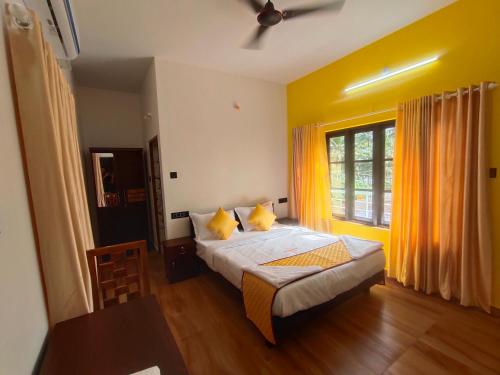 a bedroom with a bed with yellow walls and a window at Popple Beach House in Varkala
