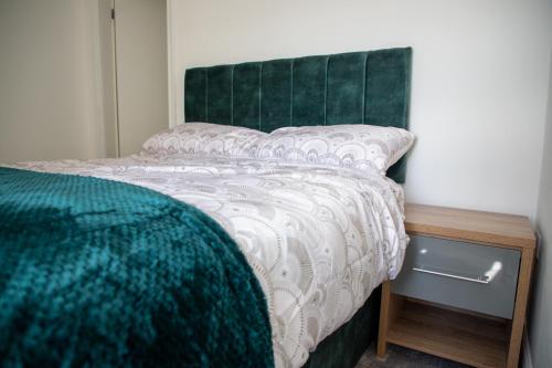 a bed with a green headboard next to a wooden night stand at Balmoral Stays 5 - Second Floor in Blackpool