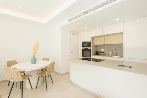 a white kitchen with a white table and chairs at Brand-new beachside apartment, with spacious terrace and exceptional amenities, in Fuengirola in Fuengirola
