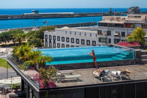a woman standing next to a swimming pool on top of a building at Savoy Insular VI by An Island Apart in Funchal