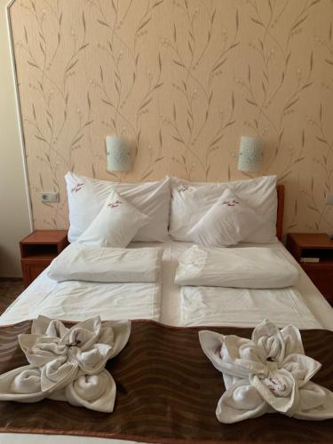 a bed with two white towels and two flowers on it at Szent István Wellness Panzió in Makó