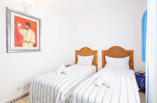 two beds in a room with a picture on the wall at Riad Asilah 32 in Asilah