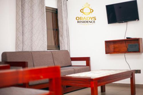 ein Wohnzimmer mit einer Couch, einem Tisch und einem Fernseher in der Unterkunft ORADYS Residence in Sanguéra