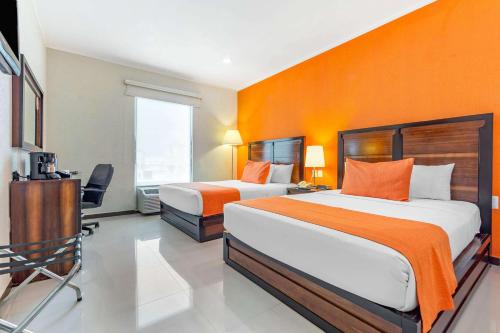 two beds in a hotel room with orange walls at Comfort Inn Cancún Aeropuerto in Cancún