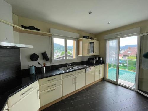 une cuisine avec des placards blancs et une grande fenêtre dans l'établissement Maison avec jardin Gérardmer L'AUTOUR, à Gérardmer