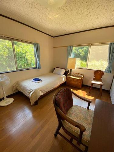 a bedroom with a bed and a chair and two windows at Grace House グレイスハウス- Country Home Relaxation in Okawa