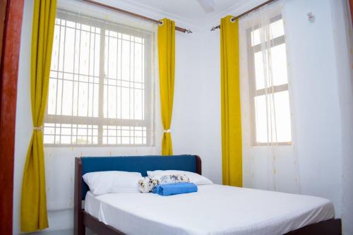 a bedroom with two windows and a bed with a blue headboard at Lux Suites Casey's Apartments Bamburi in Bamburi