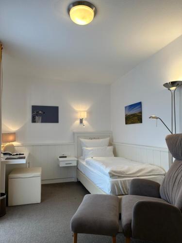 a white bedroom with a bed and a chair at Romantik Hotel Achterdiek in Juist