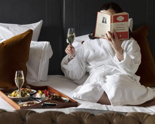a woman laying in bed reading a book and drinking wine at Kimpton Charlotte Square by IHG in Edinburgh