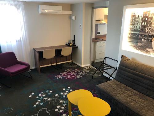 a living room with a couch and a table and chairs at Brit Hotel Caen Nord - Mémorial in Caen