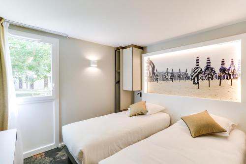 two beds in a room with a picture on the wall at Brit Hotel Caen Nord - Mémorial in Caen