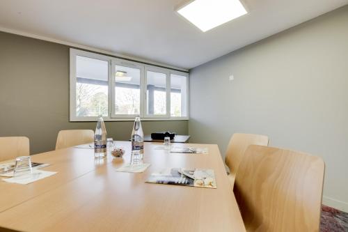 a conference room with a wooden table and two windows at Brit Hotel Caen Nord - Mémorial in Caen