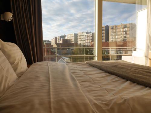 a bedroom with a bed and a large window at Hotel Maxim in De Panne