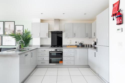 a white kitchen with white cabinets and a black appliance at 4 Bedroom House By Humming Nest Short Lets & Serviced Accommodation Milton Keynes With Free WiFi & Parking in Milton Keynes