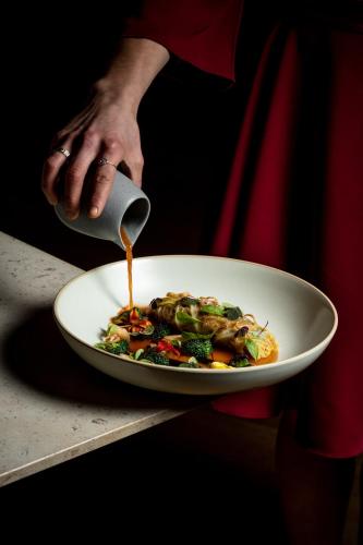 a person is pouring sauce on a plate of food at Fairmont Pacific Rim in Vancouver