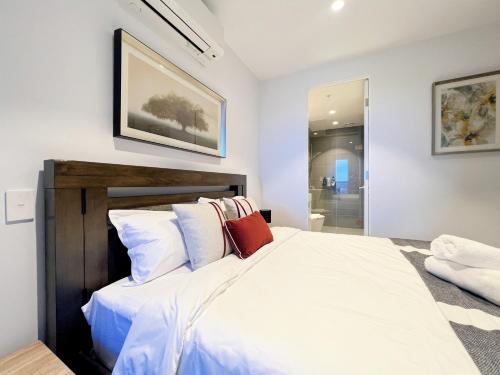 a bedroom with a bed with white sheets and red pillows at Box Hill Central Sky One Apartment in Box Hill