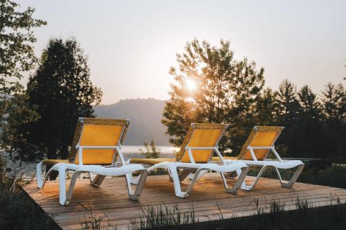 two chairs sitting on a deck with the sun in the background at Lakefront Mountain View - Resort Access Loft in Lac-Superieur