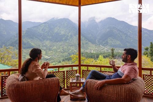 a man and woman sitting on a porch with cups of coffee at StayVista at Ruhaniyat in Pahalgām