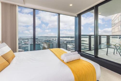 a bedroom with a large bed and large windows at Top Floor Harbour View and Skytower View Apartment in CBD in Auckland