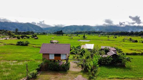 a small house in a green field with mountains in the background at DeeTorJai FarmStay Nan ดีต่อใจ ฟาร์มสเตย์ น่าน โดยเจ้าของ in Ban Klang
