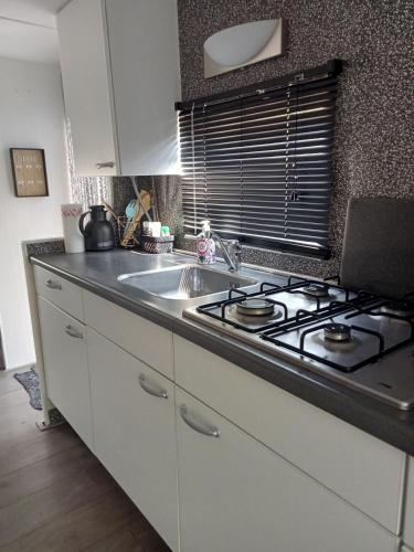a kitchen with a stove and a sink at Gezellige, knusse, Stacaravan Banjer in Schoonloo