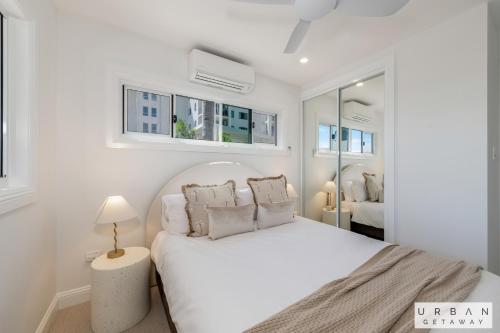a white bedroom with a large white bed with pillows at Bargara Coastal Luxe Aircon, Outside Pet, Sleeps 8 in Bargara