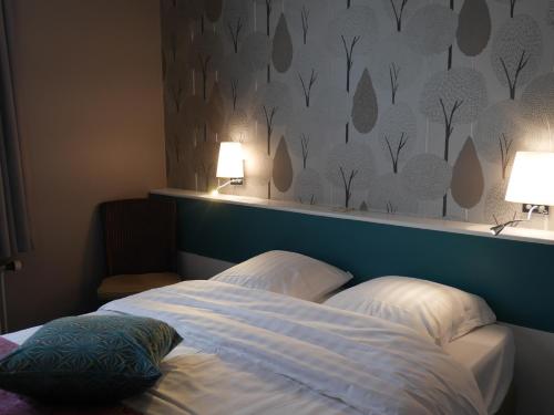 a bed with two pillows in a bedroom with two lamps at Hotel Cajou in De Panne