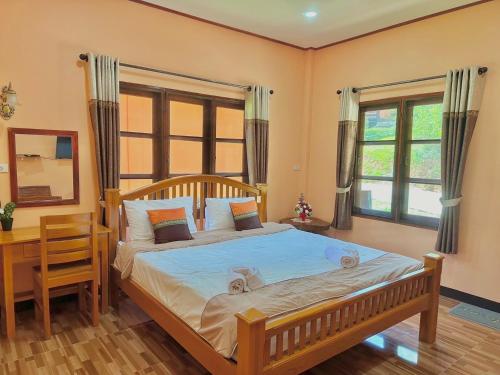 a bedroom with a bed and a desk and windows at Baanphuthadol in Mae Hong Son