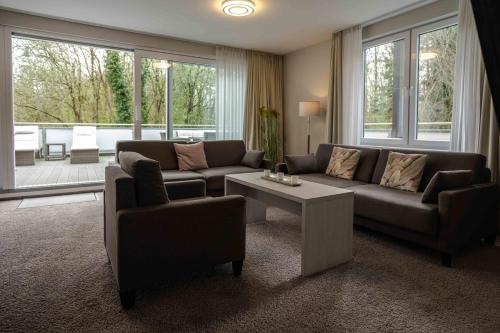 a living room with a couch and a table and windows at Hotel des Nordens Flensburg Wellness & Spa in Flensburg