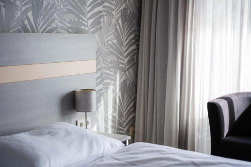 a bedroom with a bed and a chair next to a window at Hotel des Nordens Flensburg Wellness & Spa in Flensburg