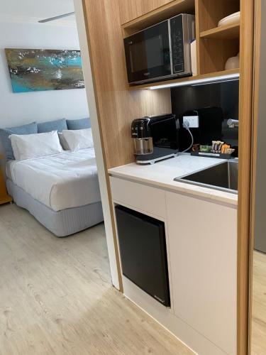 a room with a bed and a kitchen with a microwave at Redvue Holiday Apartments in Redcliffe