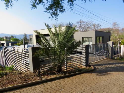 a house with a fence and a palm tree at The Executive - Exclusive Self-Catering Apartments - Ezulwini in Ezulwini