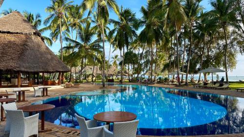 basen ze stołami, krzesłami i palmami w obiekcie Bluebay Beach Resort & Spa w mieście Kiwengwa
