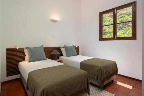 two beds in a room with a window at Casa Amarela da Fajã da Areia by An Island Apart in São Vicente
