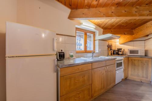 La cuisine est équipée d'un réfrigérateur blanc et de placards en bois. dans l'établissement Appartement Grand Roc 2 - 241 - Happy Rentals, à Chamonix-Mont-Blanc