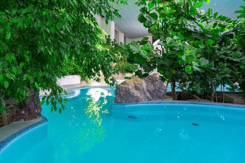 a blue swimming pool with trees and a rock at Eventhotel Pyramide in Vösendorf