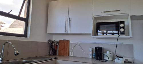 a kitchen with white cabinets and a sink and a microwave at Baleia Azul - House 7A in Ponta Mamoli