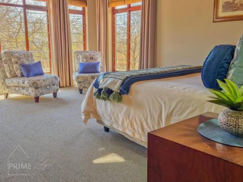 a bedroom with a bed and two chairs and windows at Rhino Lodge at Zebula in Mabula