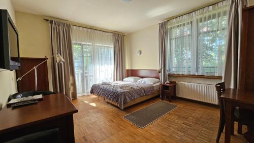 a bedroom with a bed and a desk and windows at Jasny Dwór in Polanica-Zdrój
