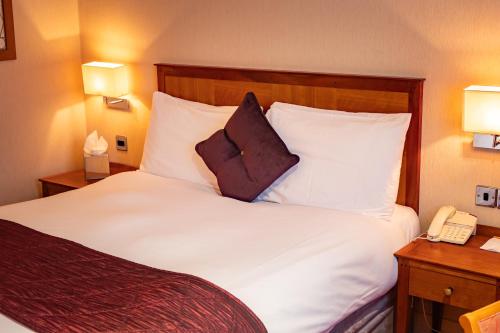 a hotel room with a bed with white sheets and a phone at The Red Lion Hotel in Hillingdon