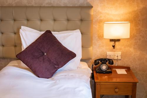 a bed with a pillow and a table with a phone at The Red Lion Hotel in Hillingdon