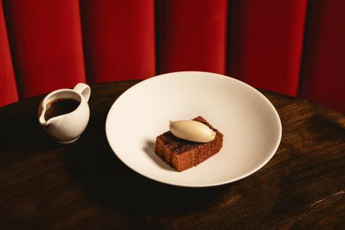 a white plate with a piece of cake and a cup of coffee at Kimpton Fitzroy London by IHG in London