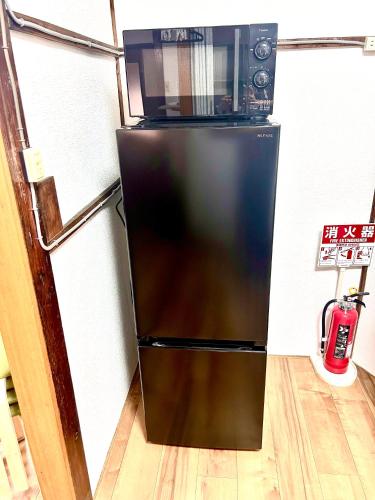 a black refrigerator with a microwave on top of it at ゲストハウスEn 折尾駅前邸 in Orio