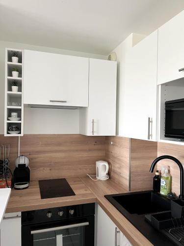 une cuisine avec des armoires blanches et un comptoir en bois dans l'établissement COSY NOISY Charmant 2 pièces entre Paris et DisneyLand, à Noisy-le-Grand
