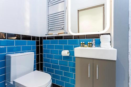 a blue tiled bathroom with a toilet and a mirror at Modern Ealing Studio Apartments, London in Ealing