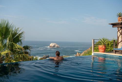 a man in a swimming pool looking at the ocean at Casa Kalmar in Zipolite