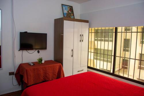 a bedroom with a red bed and a cabinet with a television at Hostal EntreOrientes in Viña del Mar