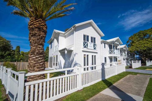 a white house with a fence and a palm tree at The Hamptons House Kiama in Kiama
